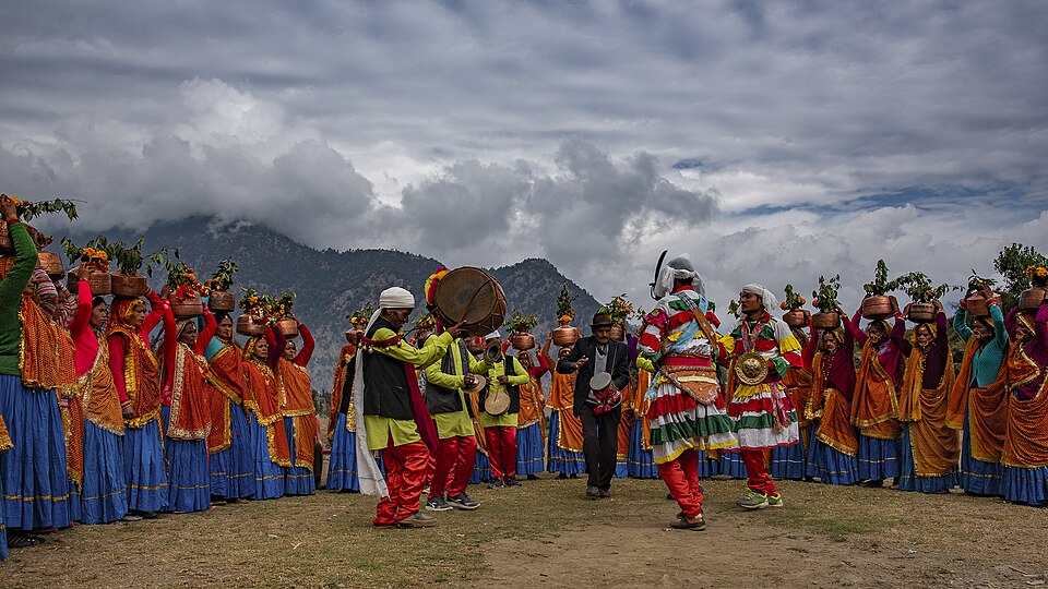 Dhol and damau players lead dancers ringed by women in traditional dress at a hill festival